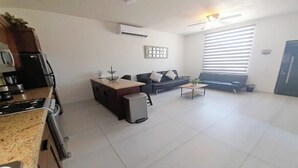 A modern kitchen with a stove, refrigerator, and a dining area with a sofa and coffee table. - Condo Casamar 3 by Kivoya (Puerto Peñasco)