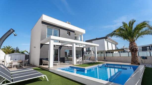Ein modernes, zweistöckiges Haus mit Pool, Sitzgelegenheit im Freien und einer Palme.