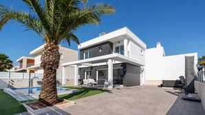 Ein modernes, zweistöckiges Haus mit Swimmingpool, Sitzgelegenheit im Freien und einer Palme.