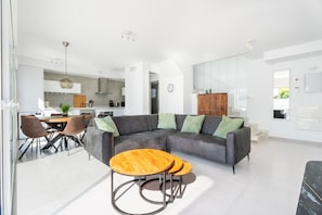 Ein modernes Wohnzimmer mit einem Ecksofa, zwei Holztischen und einem Essbereich mit Stühlen.