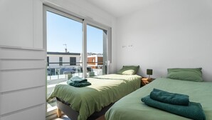 Ein Zimmer mit zwei Betten, einem großen Fenster und Blick auf Gebäude.