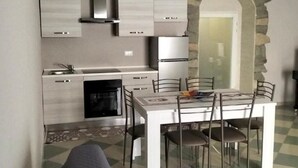 Een compacte keuken met witte kasten, een inbouwoven en een eethoek met een witte tafel en stoelen.