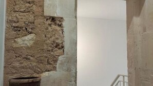 Een stenen muur met een ruwe textuur en een kleine, donkere pot erin geplaatst.