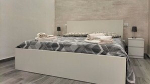 Een moderne slaapkamer met een wit bed, beddengoed met een grijs patroon en een gestructureerde grijze muur.