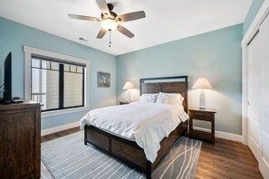 Un dormitorio con cama, mesitas de noche, ventilador de techo, ventana y puerta.