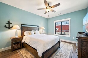 A bedroom with a bed, nightstands, a ceiling fan, a window with a view, and a decorative anchor on the wall.