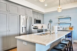 A kitchen with grey cabinets, stainless steel appliances, a marble countertop, and a bar stool area. - Marina Luxe Overlooking Sister Bay Marina (Sister Bay)