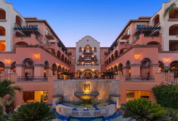 A hotel with a central courtyard featuring a fountain, multiple balconies, and warm lighting.