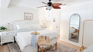 Une chambre à coucher avec un lit, des tables de chevet, un ventilateur de plafond, un miroir et un tapis.
