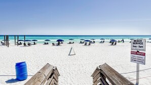 Une plage avec des chaises longues et des parasols, un panneau indiquant les heures d’ouverture du service de plage, et un avis indiquant qu’il s’agit d’une propriété privée.