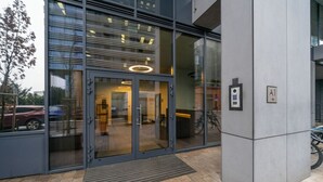 A modern building entrance with glass doors, a metal entrance mat, and a bike parking area. - Wola Apartment - 9th Floor, Parking & Balcony - by Rentujemy (Warszawa)