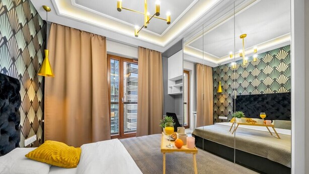 A modern hotel room with a large bed, a bedside table with breakfast items, a mirror, and a view of the city through the window. - Wola Apartment - 9th Floor, Parking & Balcony - by Rentujemy (Warszawa)