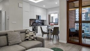 A modern apartment with a living room, dining area, kitchenette, and a balcony with a city view. - Wola Apartment - 9th Floor, Parking & Balcony - by Rentujemy (Warszawa)