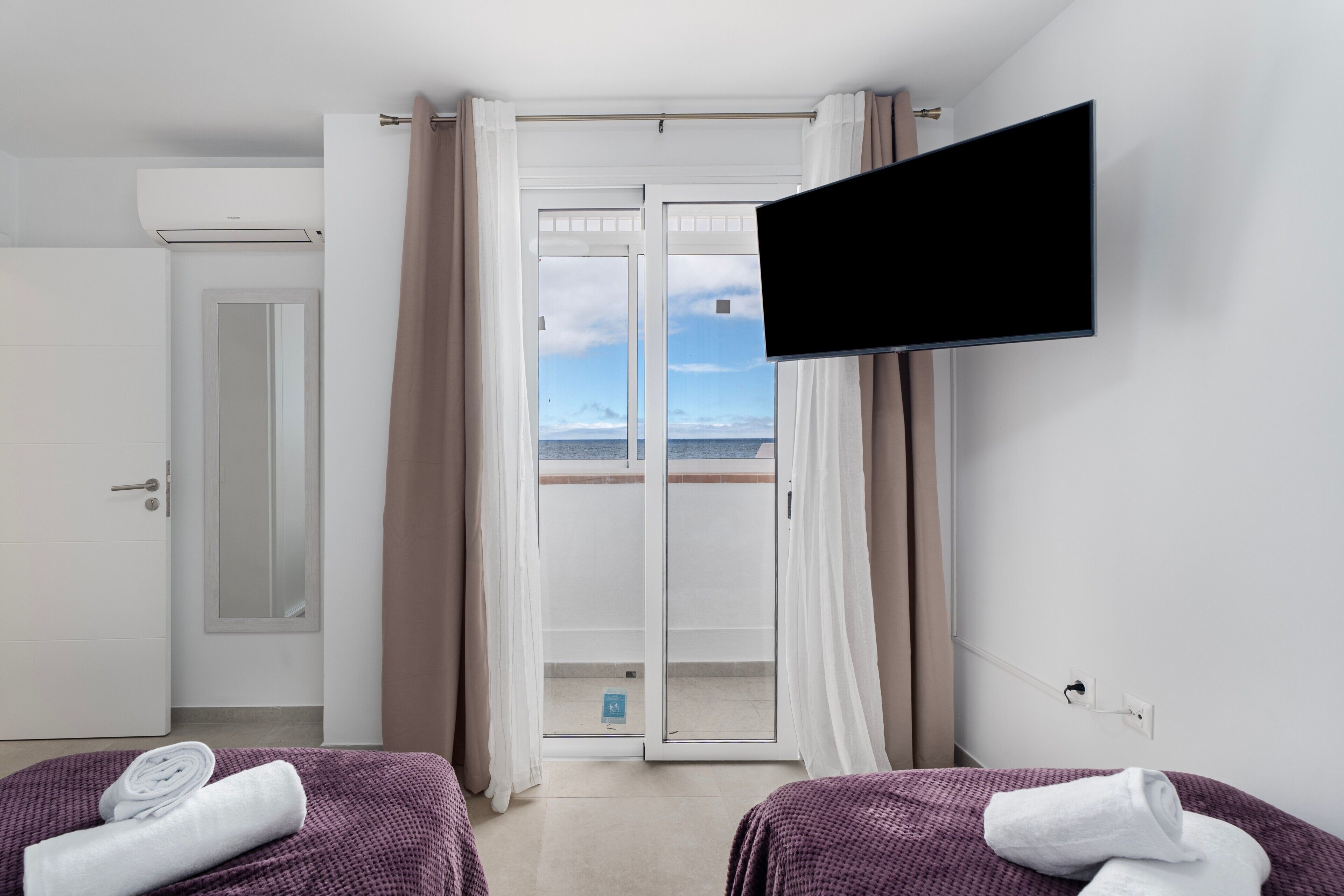Une chambre d’hôtel avec deux lits, une télévision, une porte-fenêtre coulissante donnant sur le balcon et une porte menant à la salle de bain.