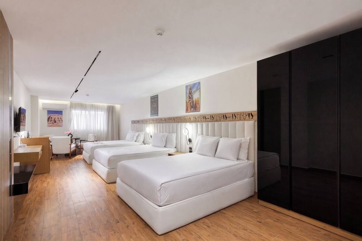 A hotel room with two beds, a desk, a chair, a wardrobe, and a large mirror.