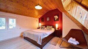 Un dormitorio con cama, una silla y techo inclinado.