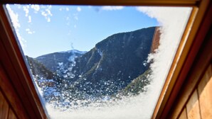 Un tragaluz con vistas a montañas nevadas y una casa.