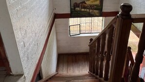Una escalera de madera con barandilla, un ventanal con reja de metal y un cuadro de caballos en la pared.