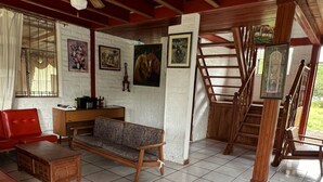 Un salón espacioso con sofá, sillas rojas, una mesa de centro de madera y una escalera que sube a un nivel superior.