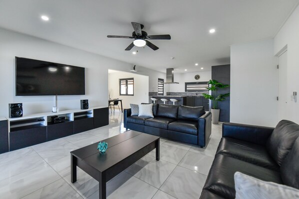 A modern living room with a black leather sofa, a coffee table, and a TV mounted on the wall.