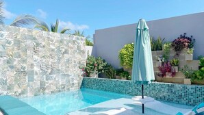 A modern outdoor swimming pool with clear blue water, surrounded by a white tiled wall and a green umbrella.