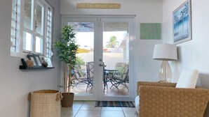 A hotel lobby with a large glass door, a potted plant, wicker furniture, and a sign above the door.