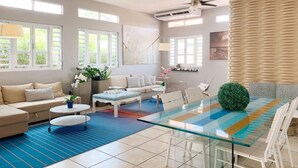 A modern living room with a glass dining table, a sofa set, a coffee table, and a large window with blinds.