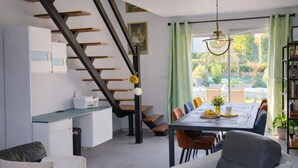 Una cocina moderna con un banco empotrado, una zona de comedor con mesa y sillas, una escalera con escalones de madera y vistas al exterior a través de amplios ventanales.