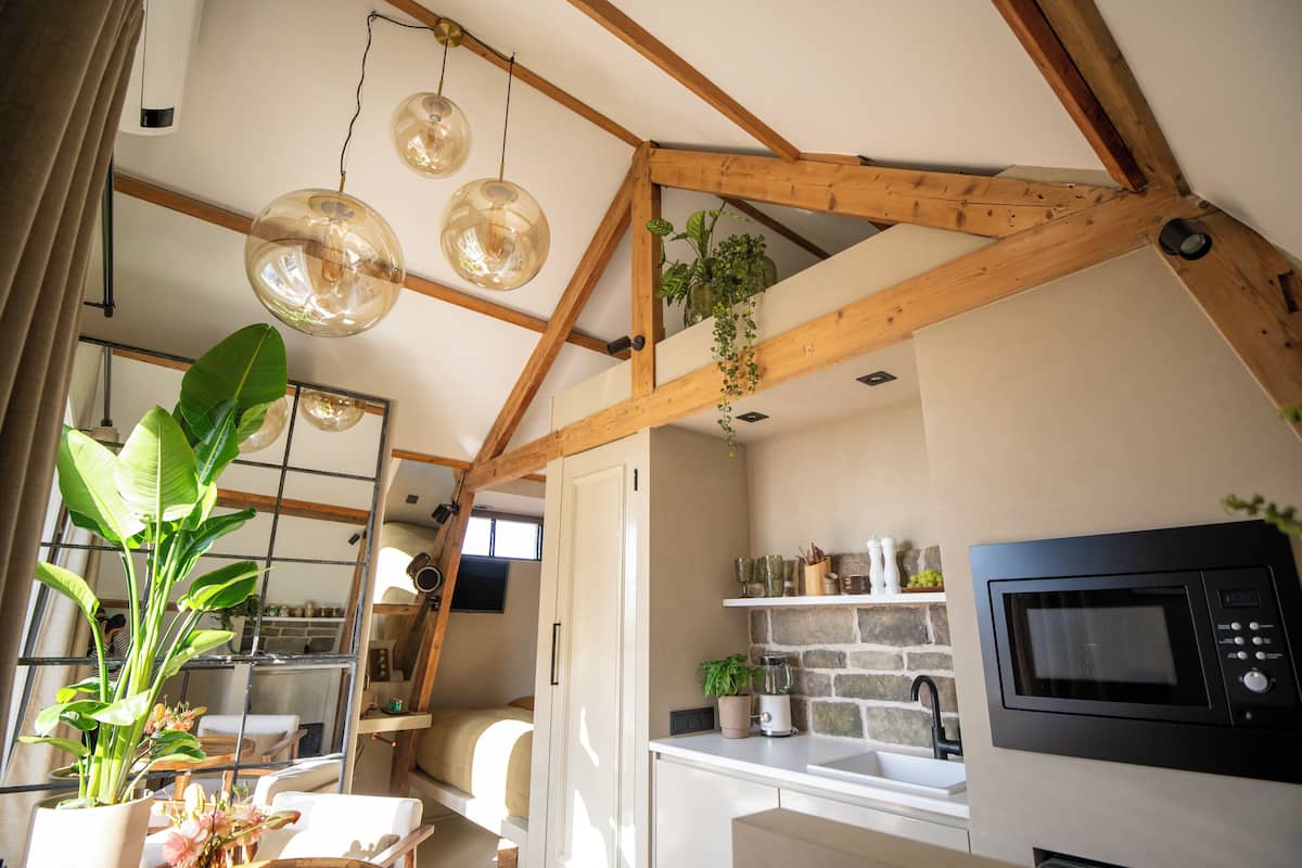 A kitchen with exposed wooden beams, a built-in microwave, and hanging pendant lights.