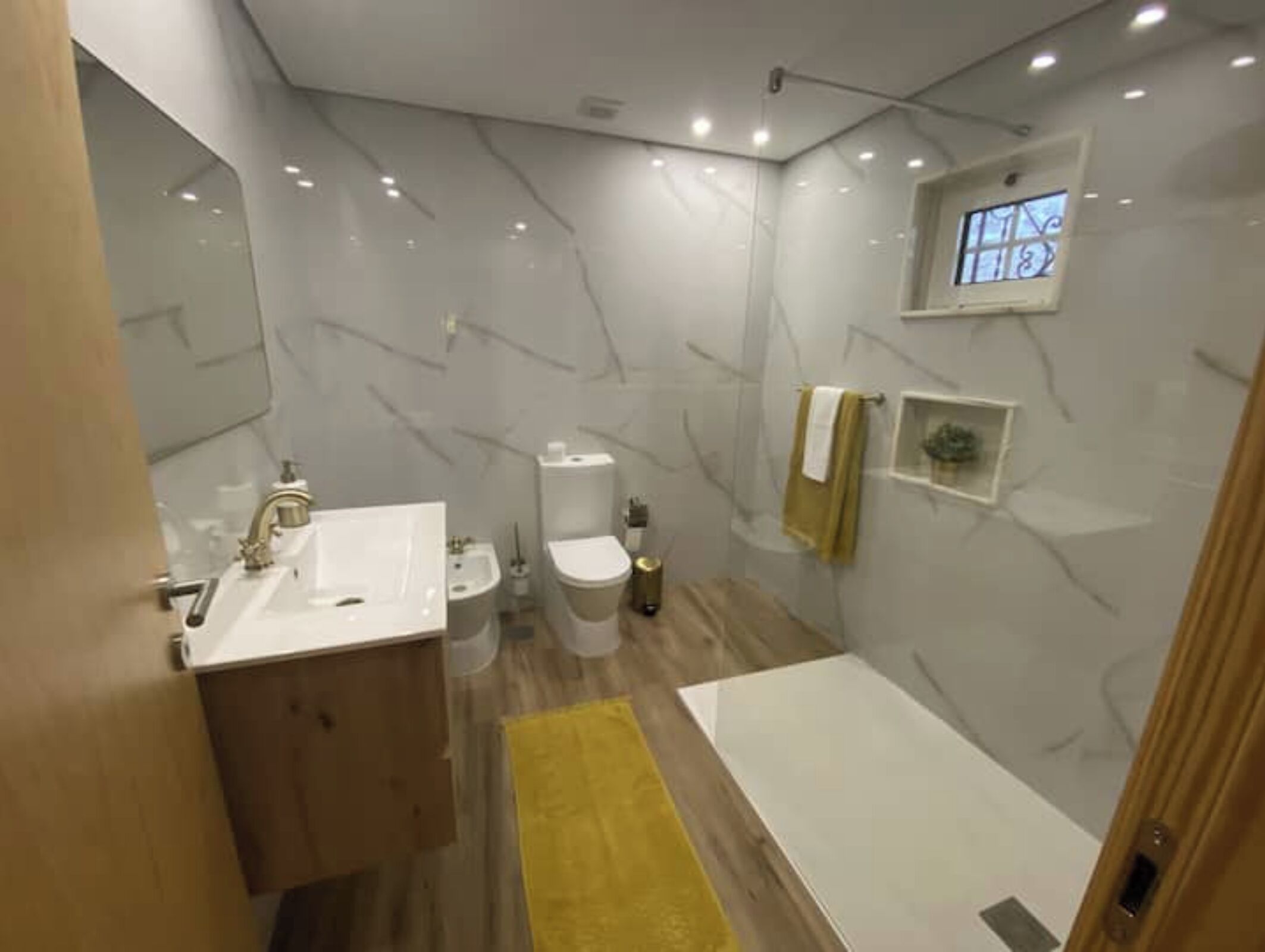Un baño moderno con pared de mármol, un lavabo, un inodoro y una bañera.