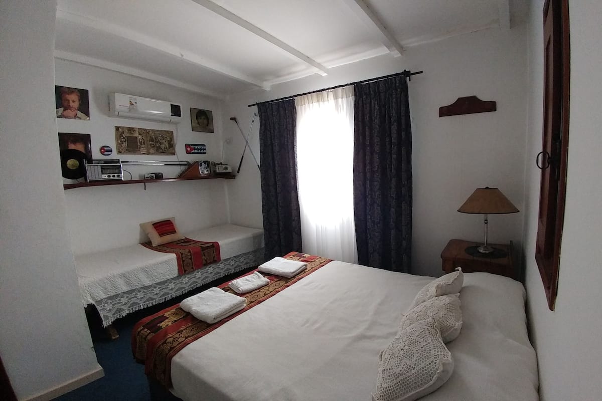 A hotel room with a bed, a small table with a lamp, a sofa, and a wall-mounted shelf with various items.