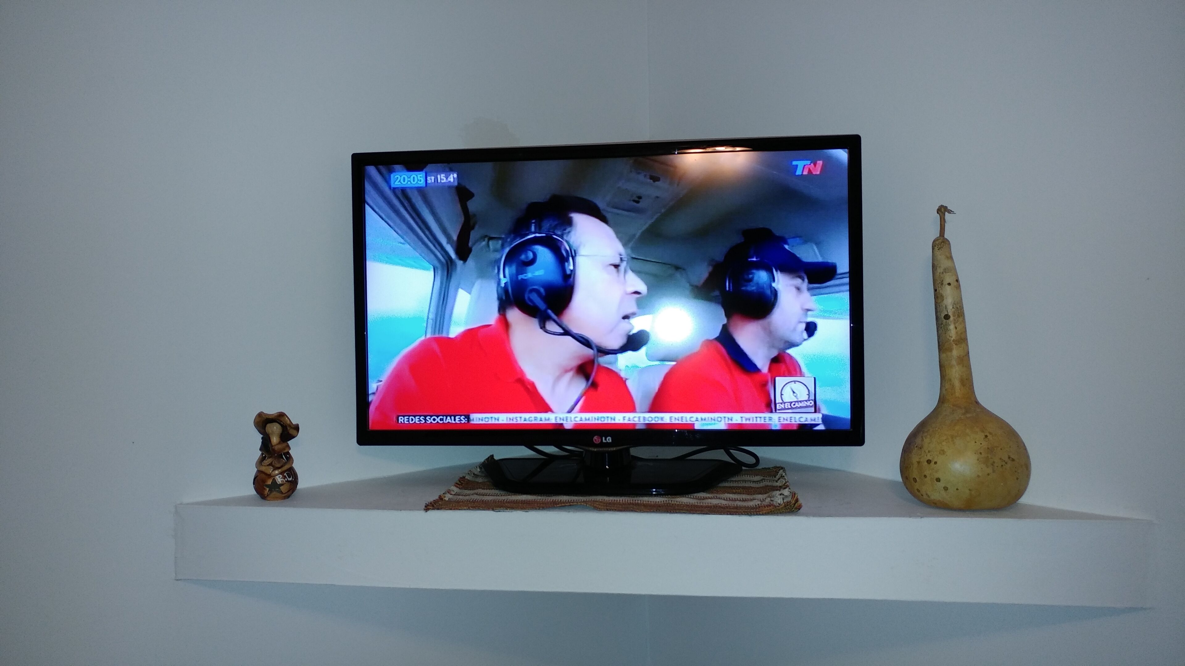 Un téléviseur posé sur une étagère blanche, diffusant une émission sportive avec deux commentateurs.