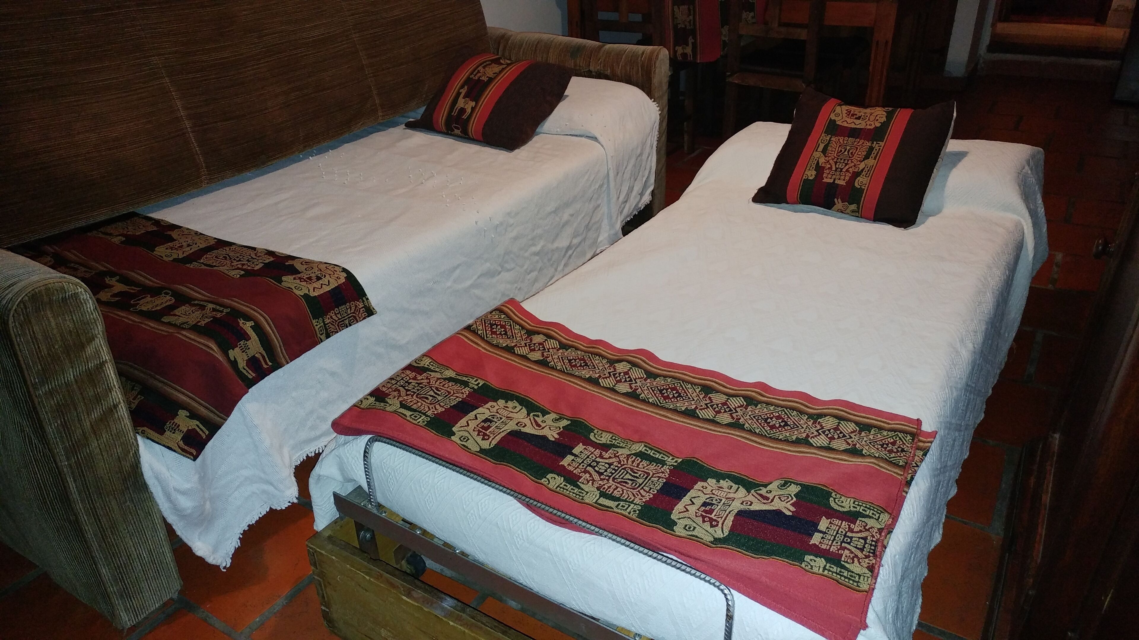 Two single beds with white linens and decorative pillows, a wooden chest, and a brown sofa.