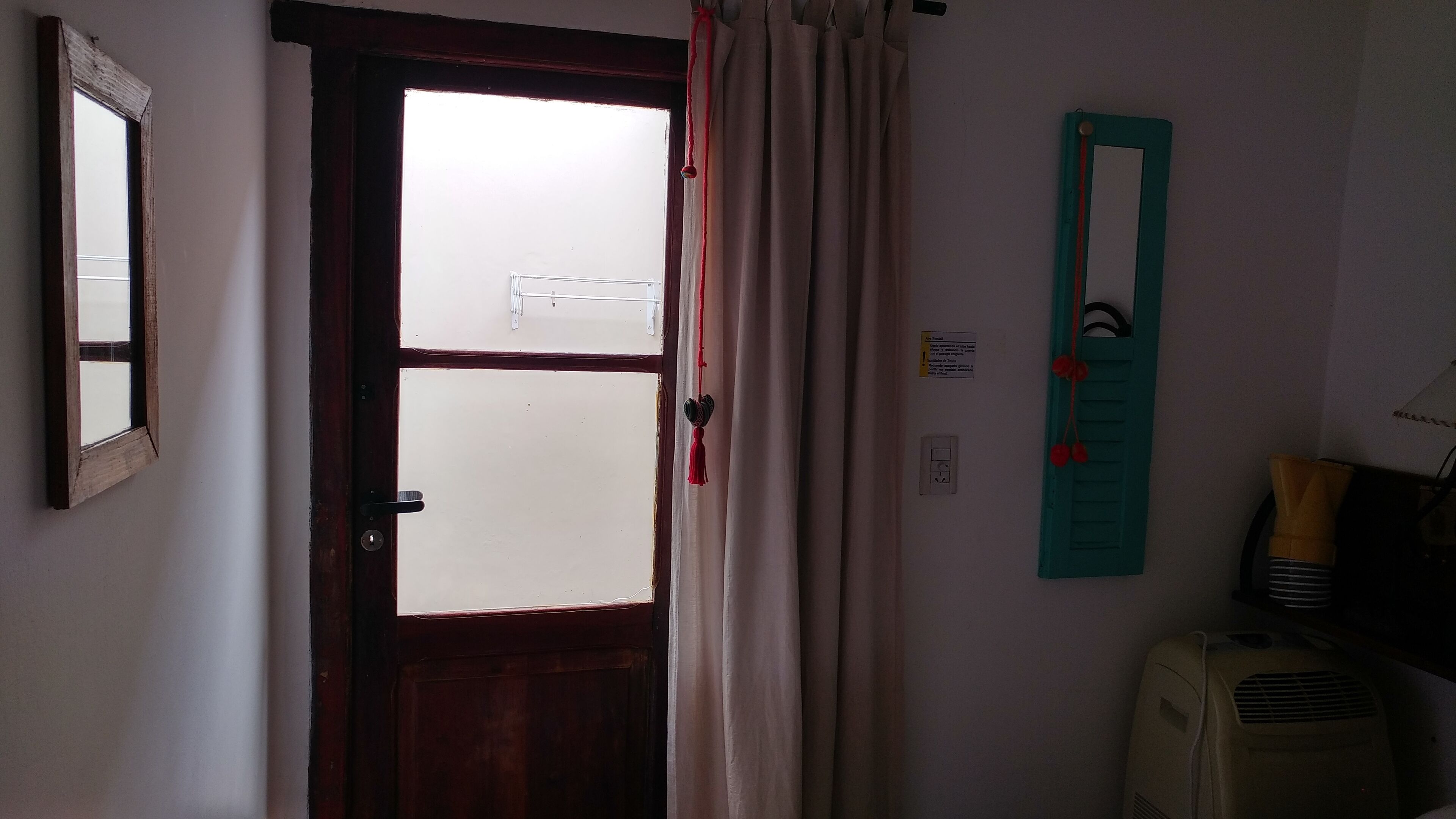 A room with a wooden door, a window with frosted glass, a teal-colored wall-mounted object, and a white air conditioning unit.