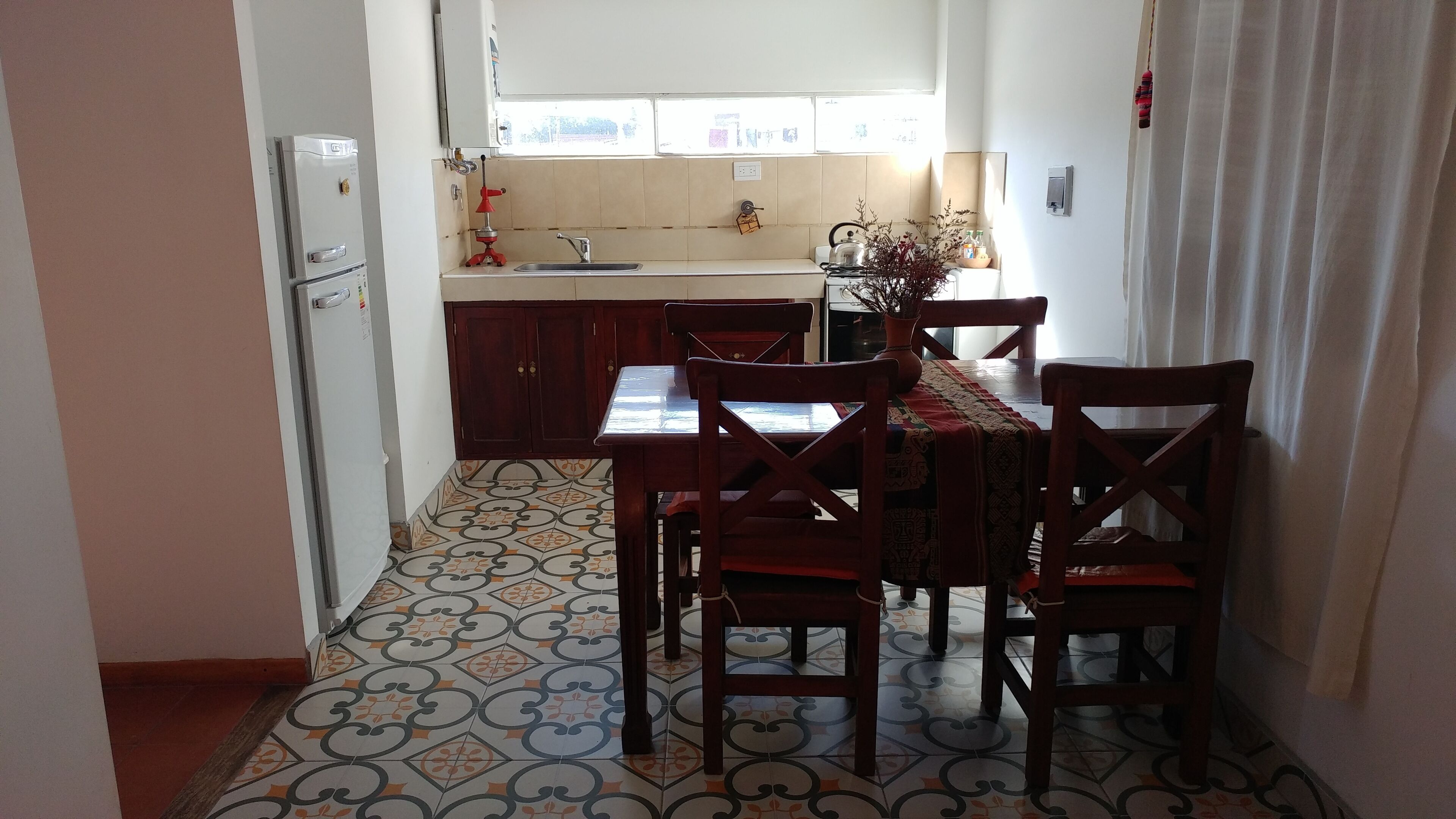 Cocina compacta con mesa y sillas, refrigerador, pileta y ventana con vistas.