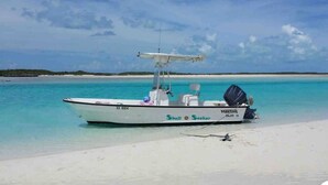 A boat named 'Maritime Skiff 18' with a cabin and outboard motor, docked on a sandy beach with clear turquoise water and a distant shoreline. - Seashore Sleeps Book Your Winter Getaway Now! (Black Point)