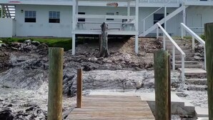 A white building with a green roof, a covered outdoor area, and a wooden staircase leading to a deck. - Seashore Sleeps Book Your Winter Getaway Now! (Black Point)