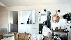 En stue med en brun lædersofa, et sofabord med en billedramme og en plante, samt et køkken, der kan ses gennem en hvælving.