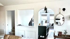 En stue med sofa, sofabord og spejl. Der er en trappe til en etage ovenpå.