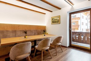 A dining area with a wooden table, cushioned chairs, a potted plant, and a painting on the wall. - Apartment 'Christa' with Mountain View, Shared Garden and Wi-Fi (Selva di Val Gardena)