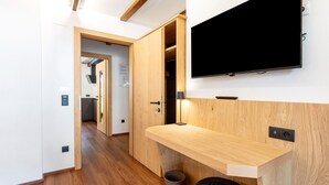 Un interior moderno con un escritorio de madera, un televisor montado y un pasillo que conduce a una zona de cocina.