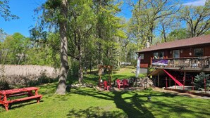 A rustic cabin with a deck and picnic table in a wooded area.