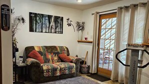 A living room with a patterned sofa, a treadmill, and a large window with curtains.