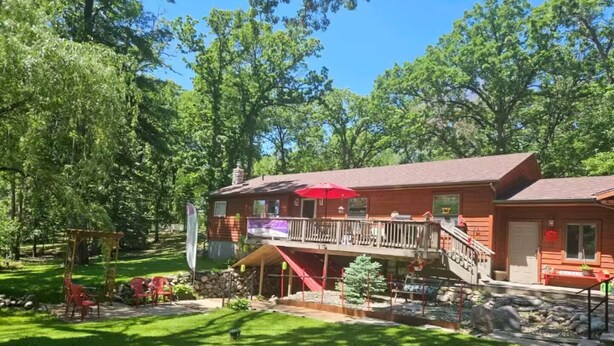 A two-story wooden cabin with a balcony, surrounded by a well-maintained lawn and trees.