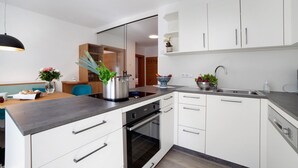 Une cuisine moderne avec des meubles blancs, un plan de travail noir, un four encastré et un coin repas comprenant une table et des chaises.