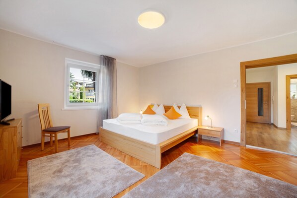 A bedroom with a bed, a chair, a desk, a TV, and a window.