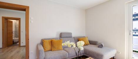 Una sala de estar moderna con un sofá gris, piso de madera y una orquídea en maceta.