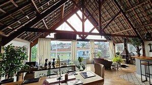 A spacious living area with a high ceiling, large windows, and a view of buildings outside. There is a bar area with stools and a variety of plants. - Private Room. SP Expo, Itaú, IBC, Congonhas, Zoo (São Paulo)