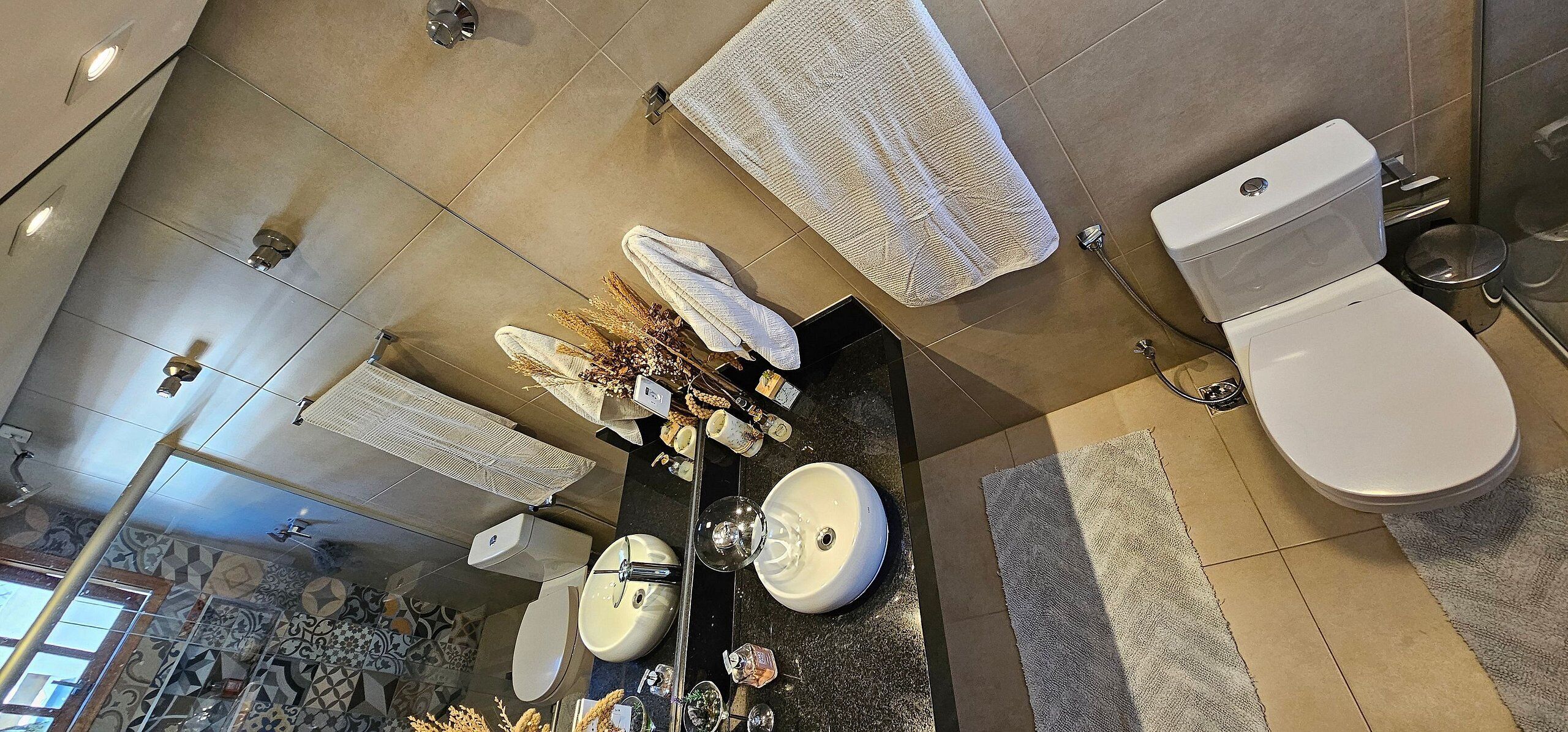 A modern bathroom with a large mirror, two sinks, a toilet, and a shower.