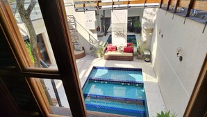 An outdoor swimming pool area with a wicker sofa and red cushions, surrounded by potted plants and a white wall. - Private Room. SP Expo, Itaú, IBC, Congonhas, Zoo (São Paulo)